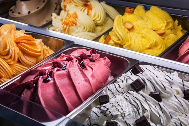 Display case of artisan gelato — strawberry, stracciatella, mango, orange, lemon — under glass